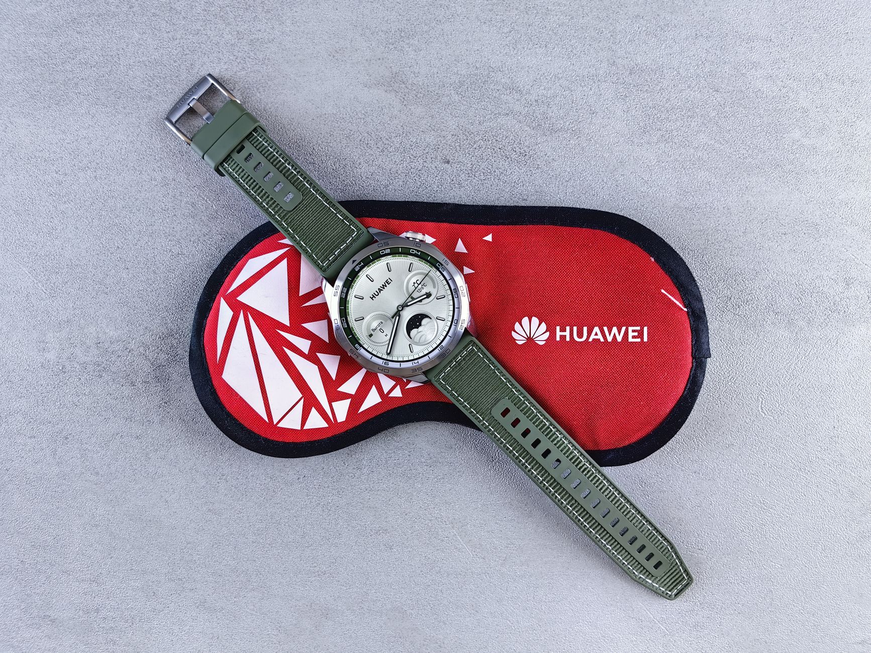 Top view of a Huawei smartwatch with green straps displayed on a red protective case. Perfect for tech enthusiasts.