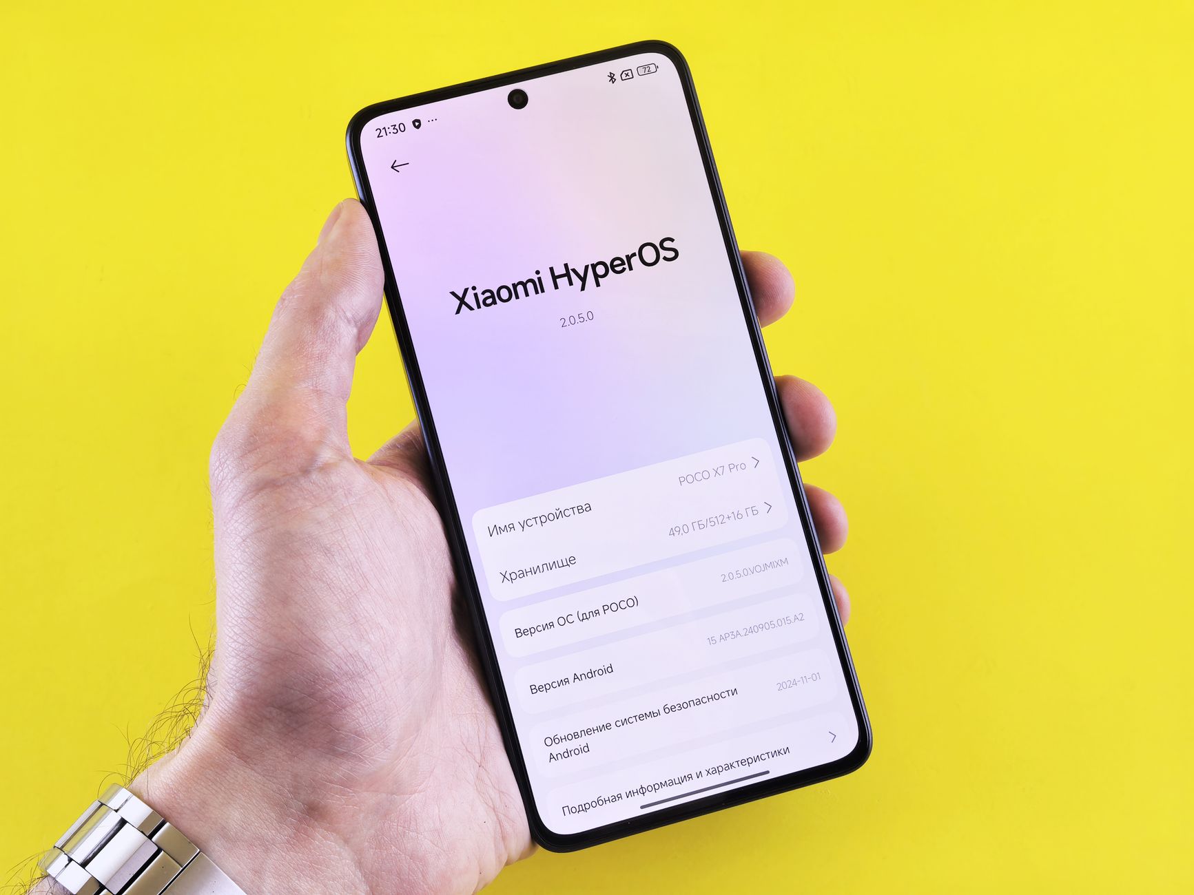 Close-up of a smartphone displaying Xiaomi HyperOS interface, held by a hand against a bright yellow background.