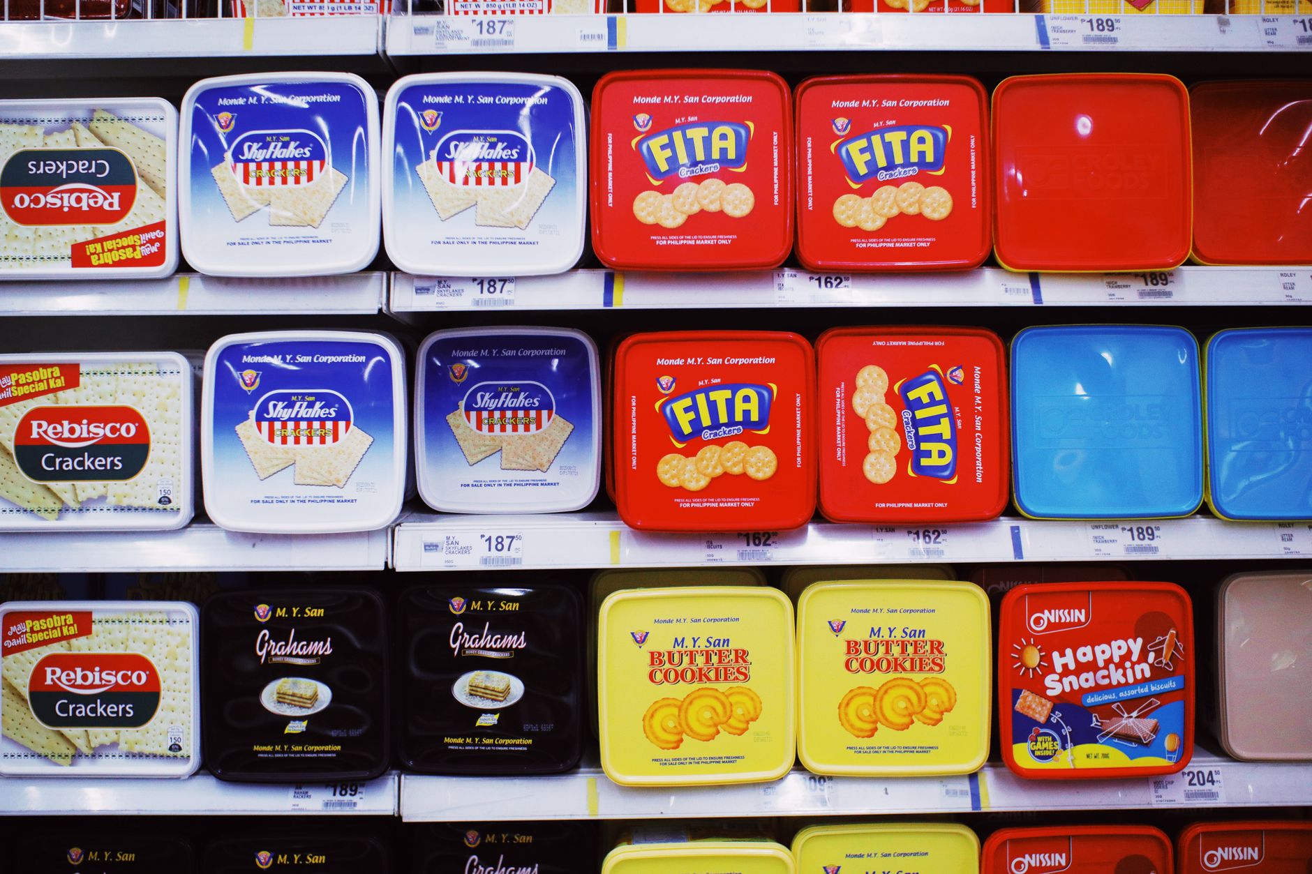 Assorted colorful boxes of tasty sweet cookies placed on shelves with prices in supermarket