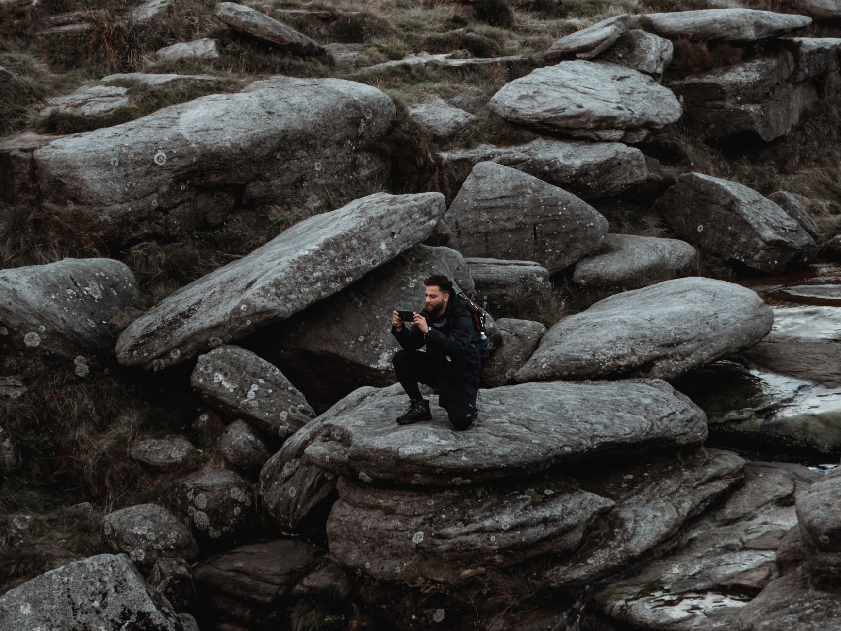 A man captures scenic rocky terrain on his smartphone while hiking in rural nature.