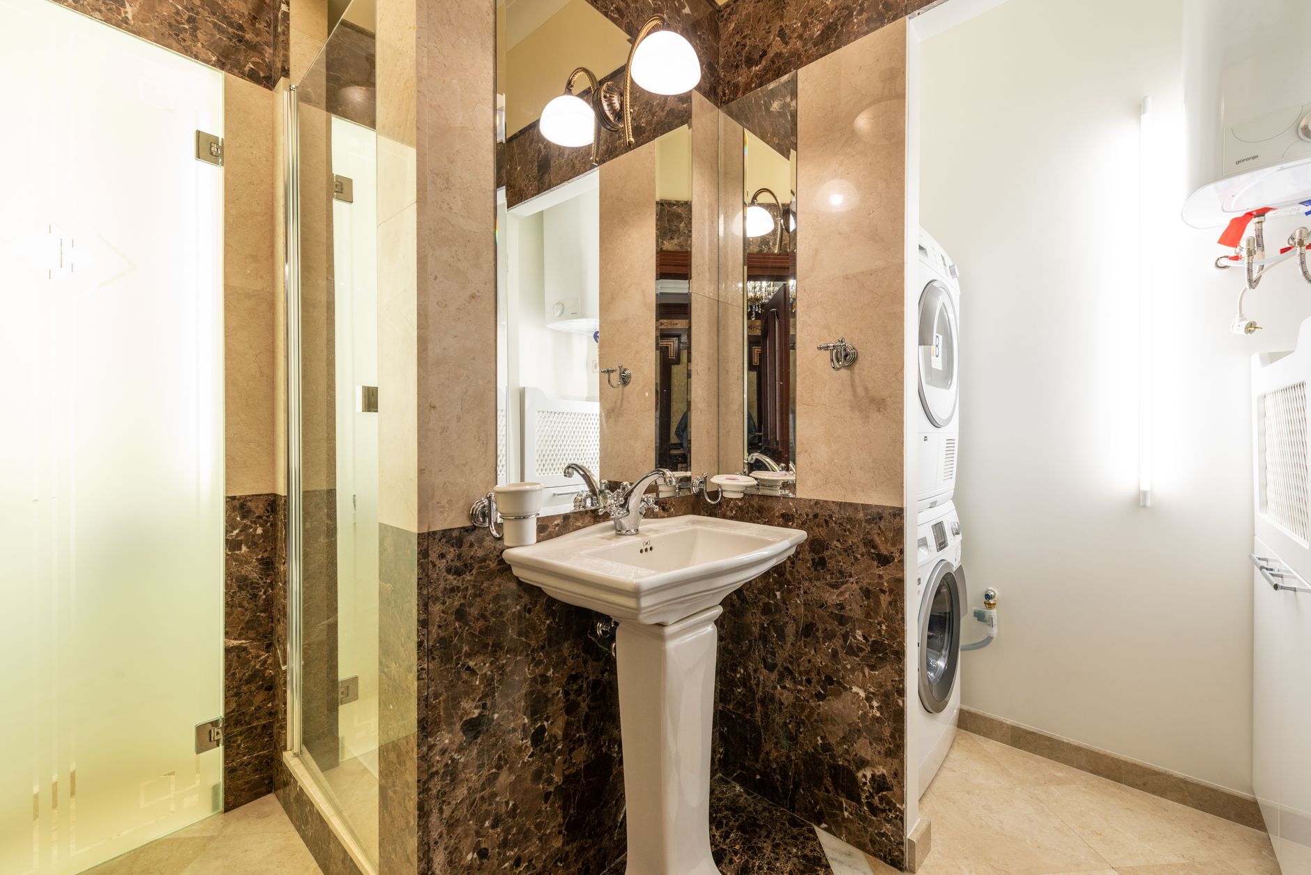 Elegant bathroom interior featuring marble walls, a pedestal sink, and a washer-dryer unit.