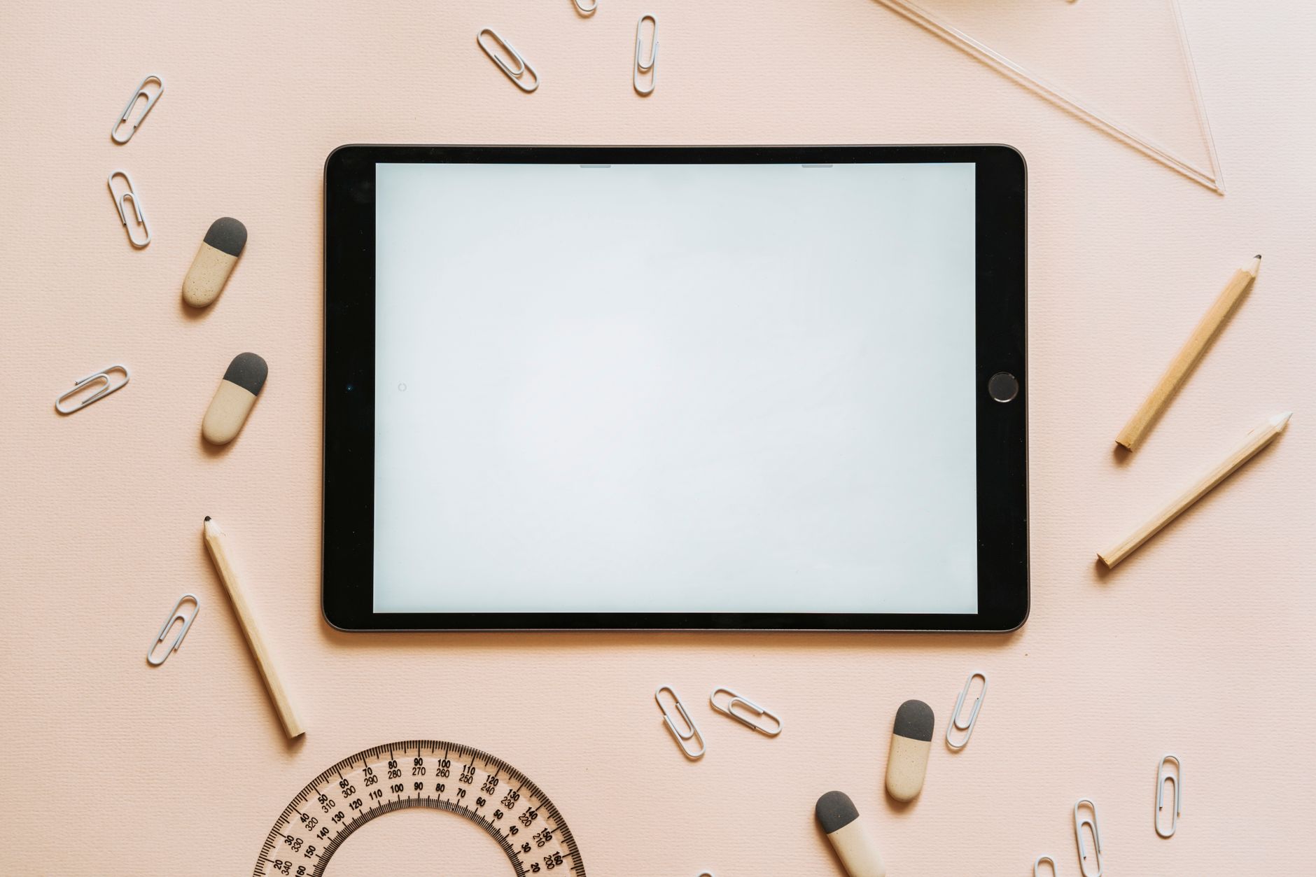A tablet surrounded by stationery items like pencils, erasers, and paper clips in a flat lay setup.