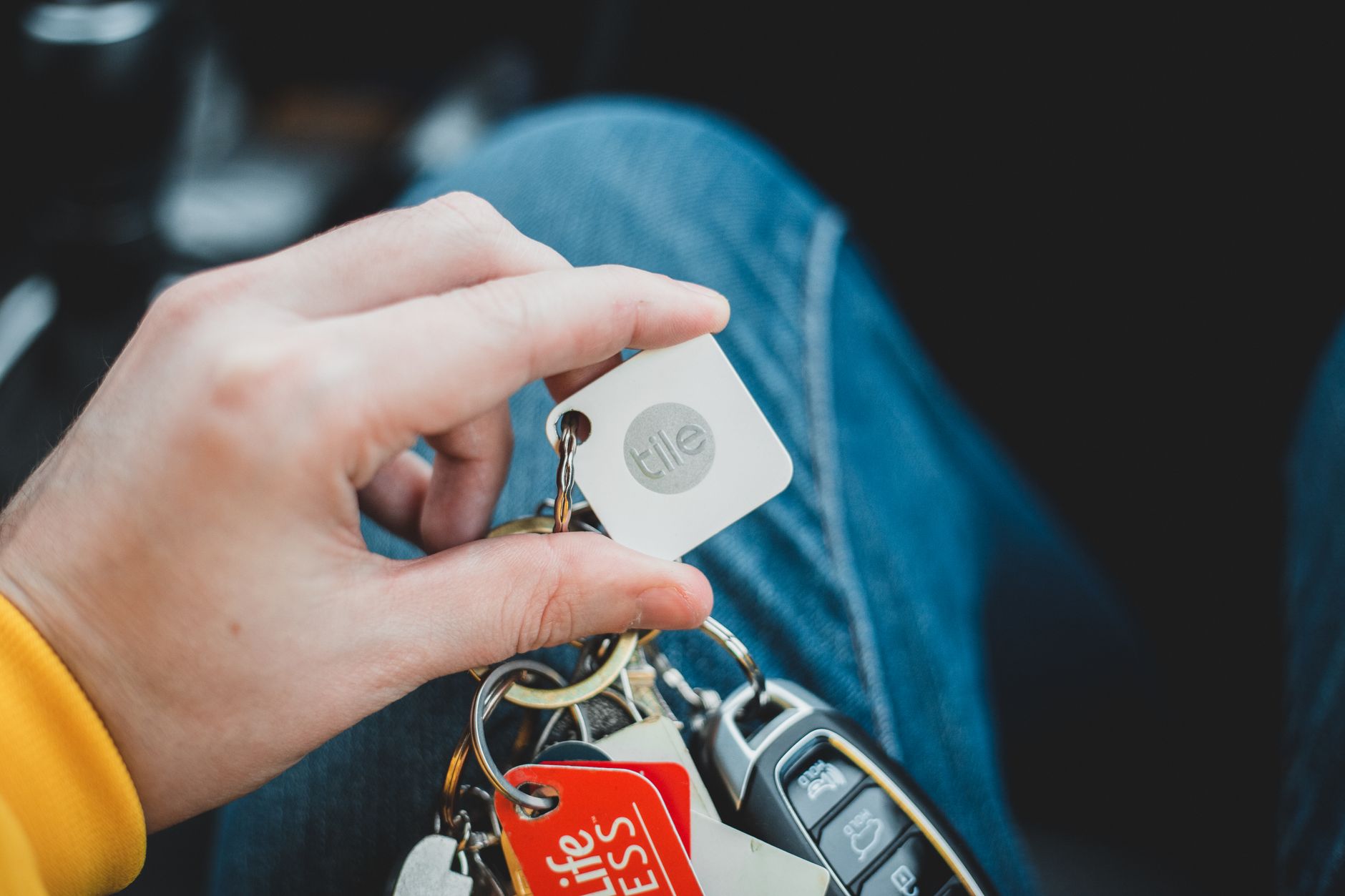 A close-up of a hand holding a set of car keys with various keychains and tags. Indoor setting.