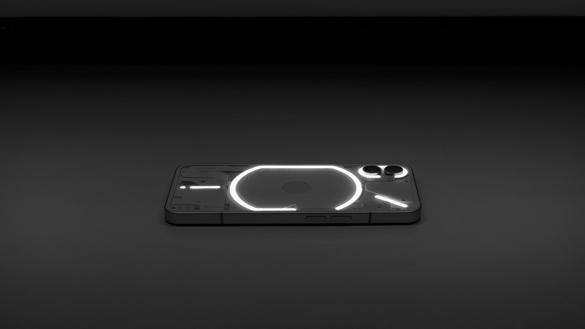 Minimalist photo of a glowing smartphone with a transparent back design on a dark surface.