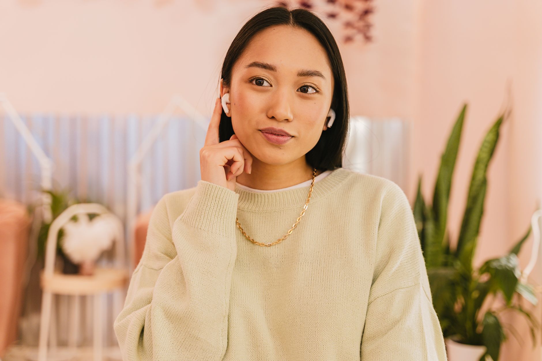 Close-up of a young woman wearing wireless earbuds, indoors with plants.