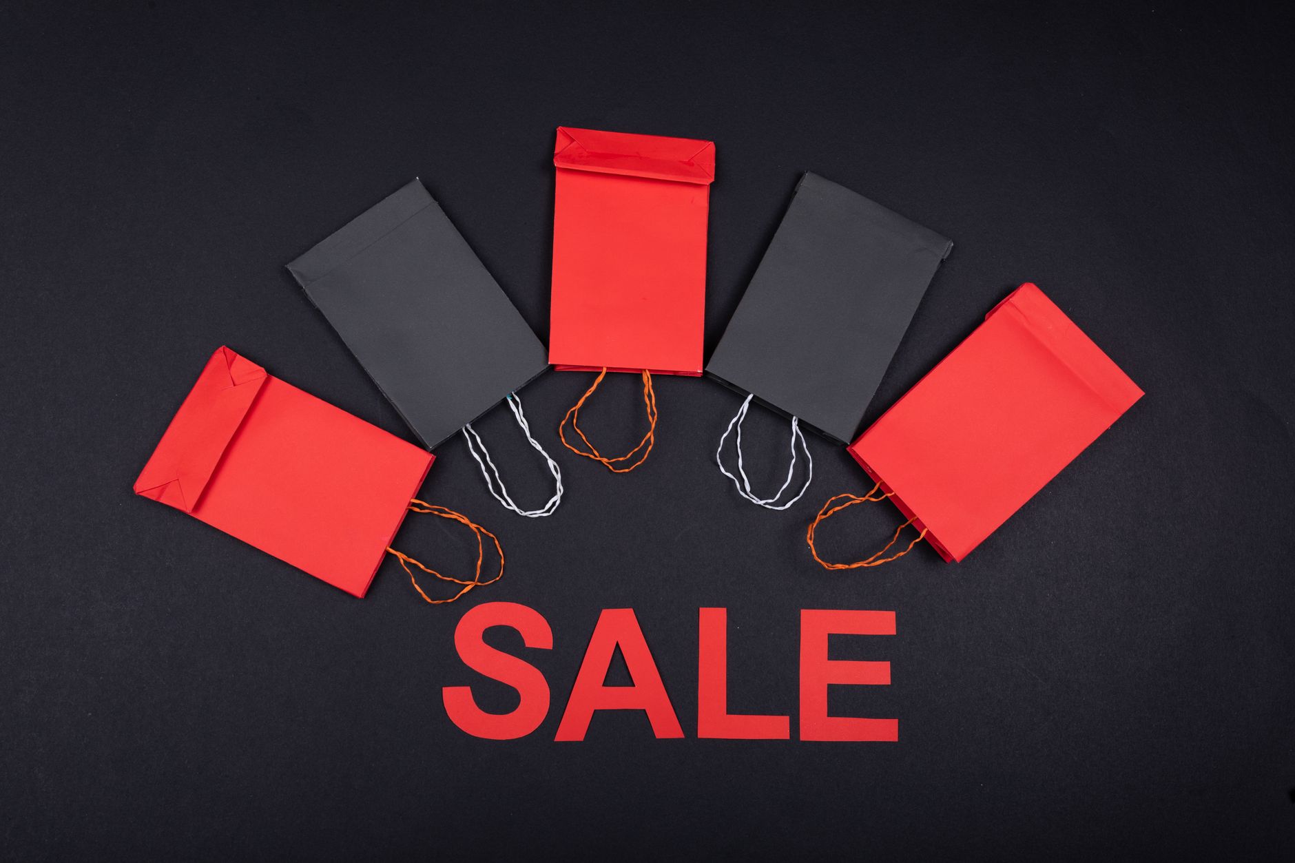 Flatlay of red and black shopping bags arranged on black background with 'SALE' text.