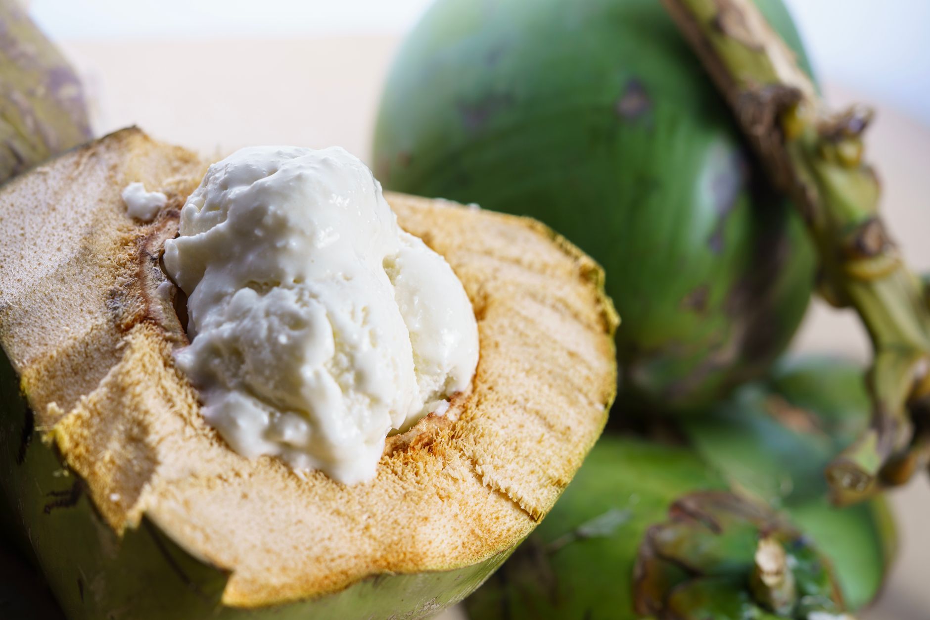 Close-up of creamy coconut ice cream served in a green coconut shell with fresh coconuts in the background.