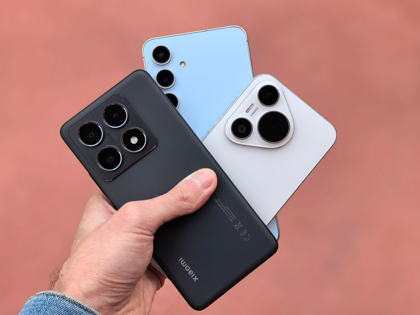 Close-up of a hand holding three modern smartphones with cameras in view, showcasing contemporary design.