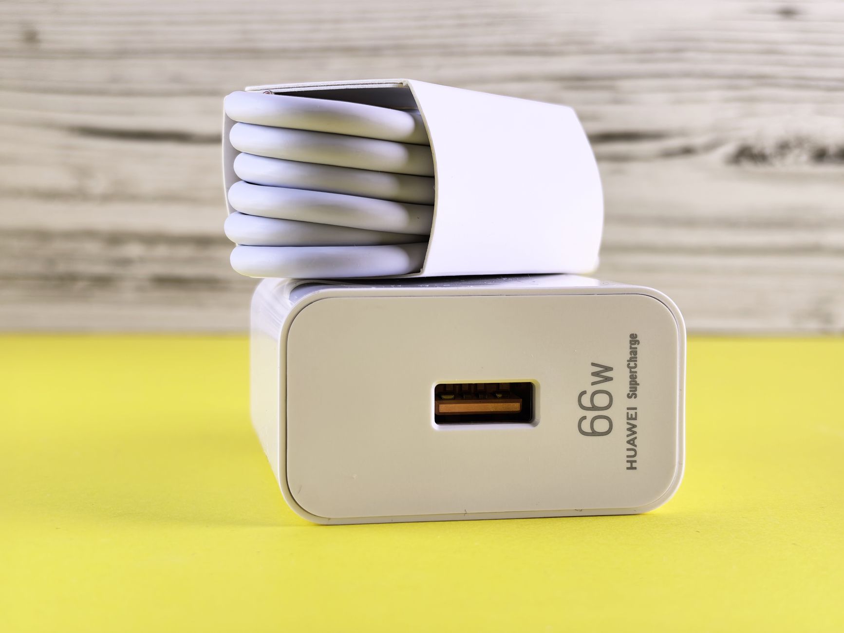 Close-up of 66W USB charger with coiled cable on a vibrant yellow surface.