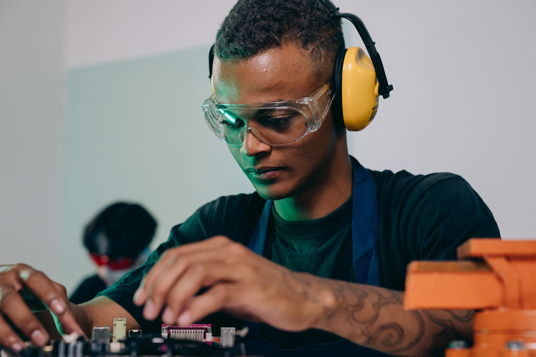 Focused young engineer repairing electronics indoors while wearing safety gear, showcasing precision and expertise.