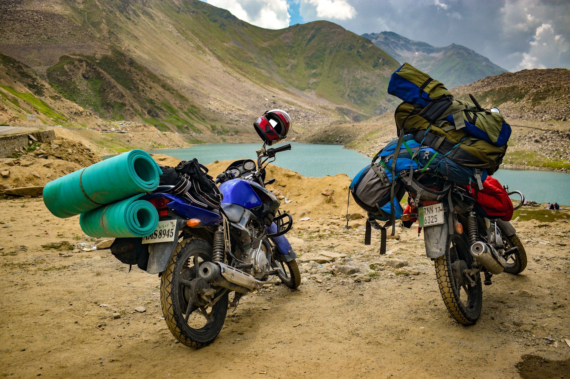 Motorbikes with camping gear parked by a scenic mountain lake, ideal for adventure and travel themes.