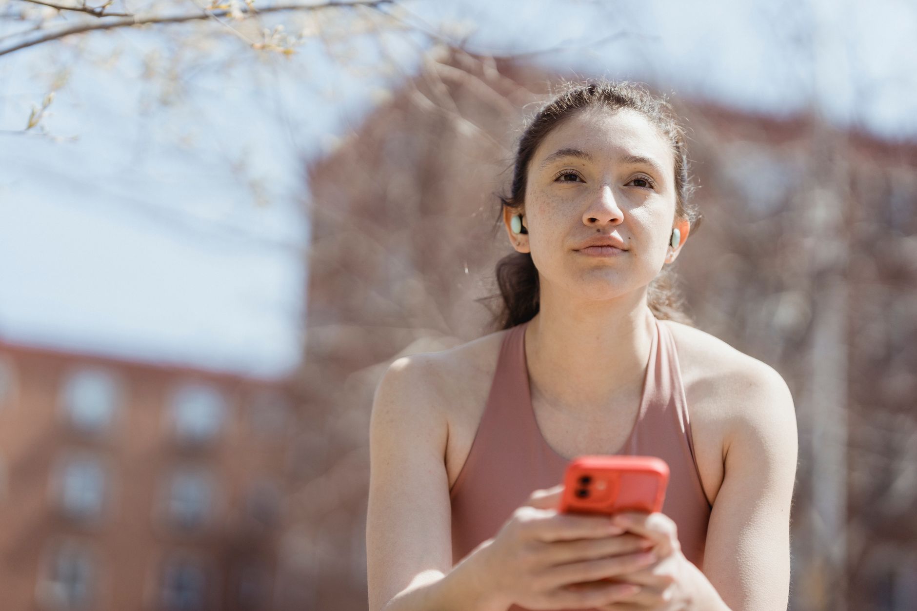 Young woman with earbuds using her smartphone outside on a sunny day.