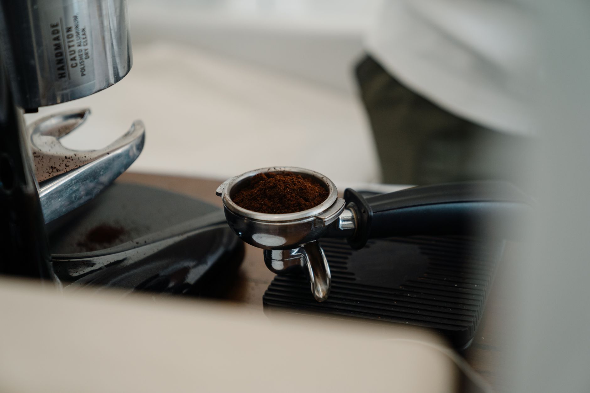 Portafilter with black holder and basket full of ground coffee placed on professional coffee machine in modern cafe kitchen